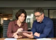 Two professionals review information on a tablet in a modern office while discussing Salesforce Implementation in Salt Lake City, UT.